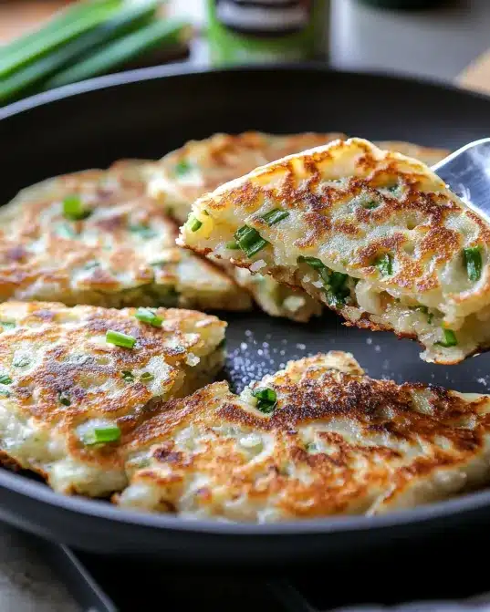 Trader Joe's Scallion Pancakes sizzling in a frying pan with golden-brown edges and green onion layers